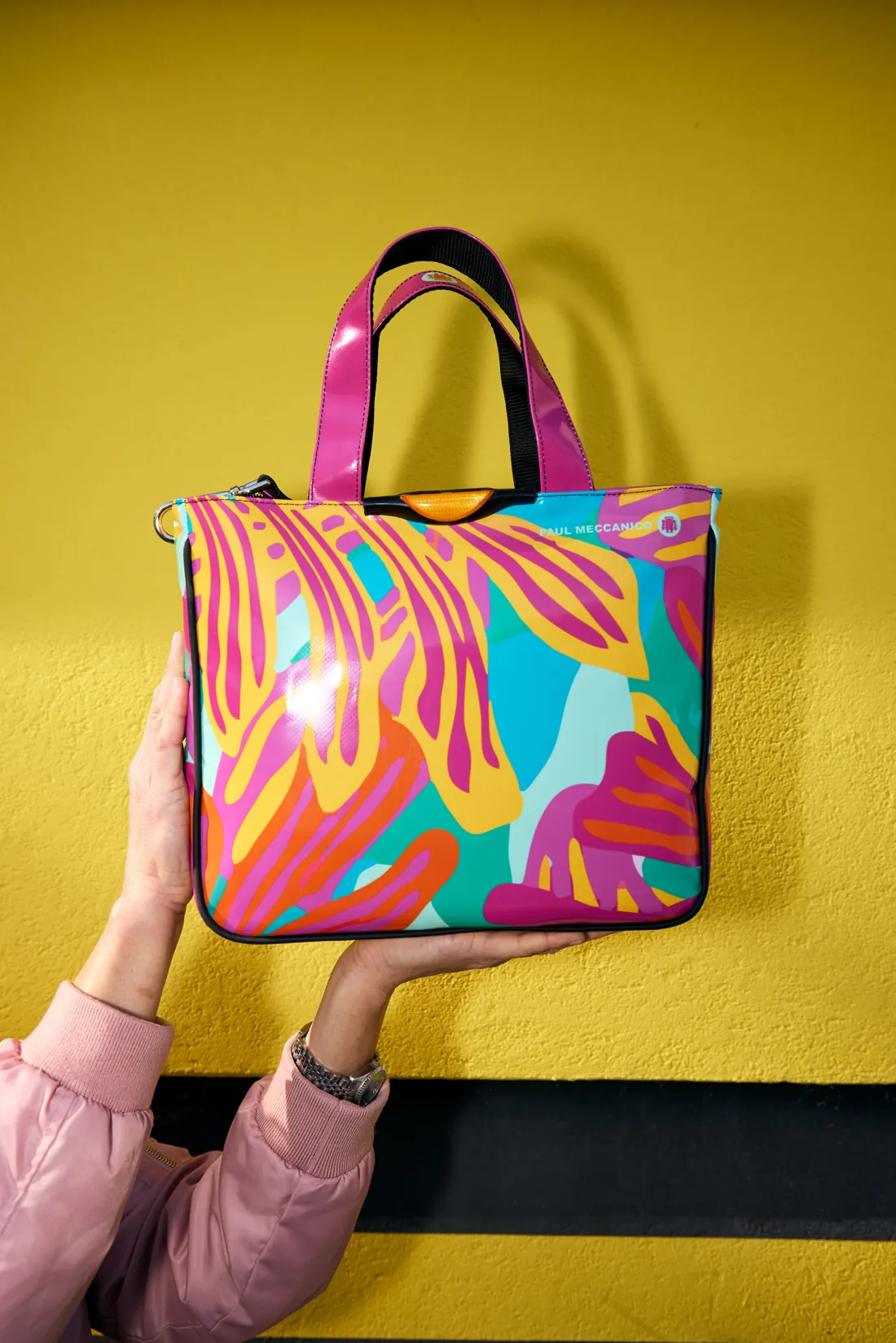 A colourful Paul Meccanico tote held up against a yellow wall